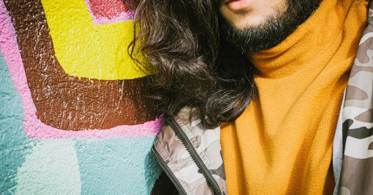 Un portrait en gros plan d'un homme à la mode avec de longs cheveux devant un mur de graffiti vibrant.