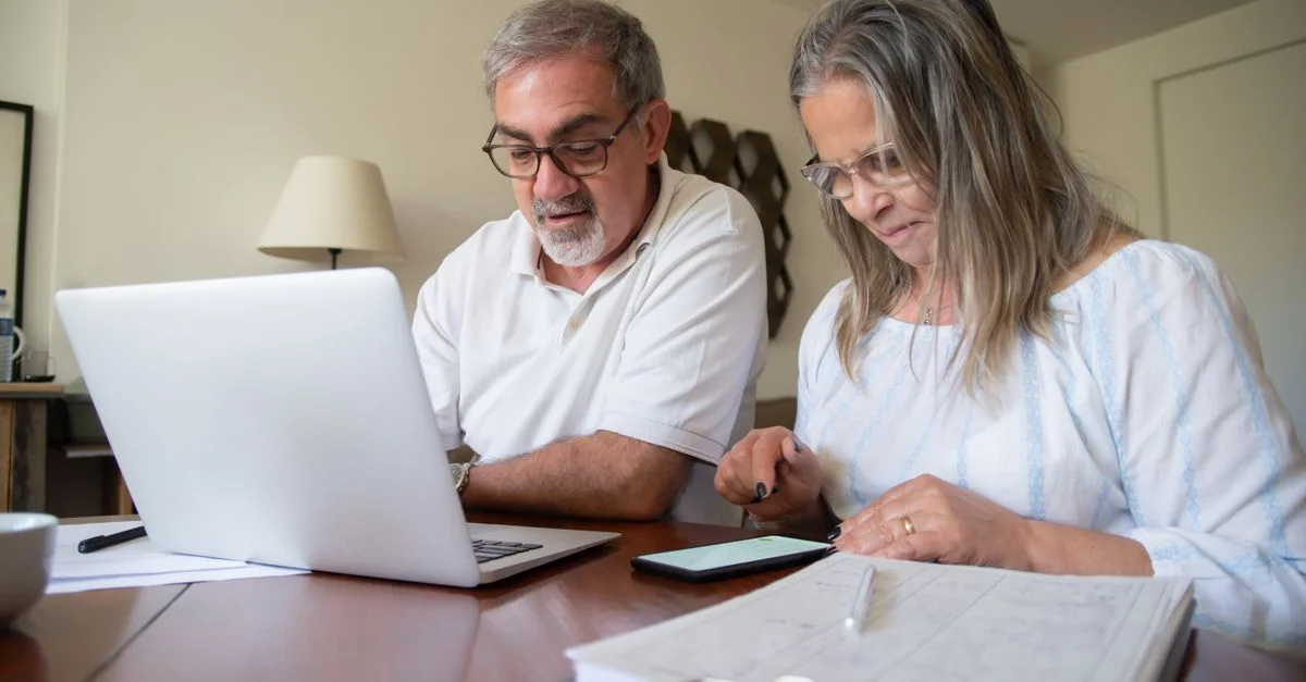 Couple âgé travaillant ensemble sur des documents avec un ordinateur portable et un téléphone à la maison.