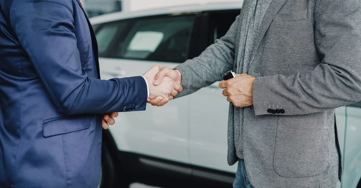 Deux hommes d'affaires se serrent la main dans une concession automobile, concluant un accord.