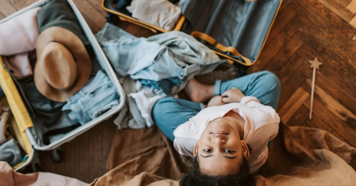 Jeune enfant entouré de vêtements et d'une valise ouverte, préparant un voyage à l'intérieur.