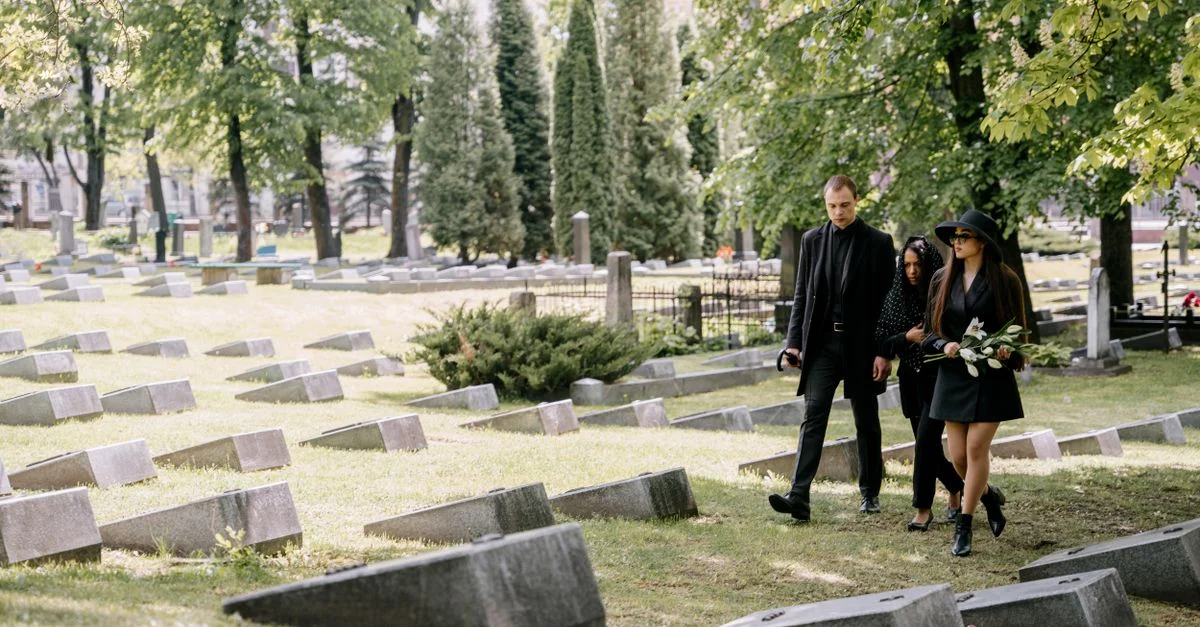 Des endeuillés marchent à travers un cimetière serein entouré d'arbres verdoyants, montrant respect et réflexion.